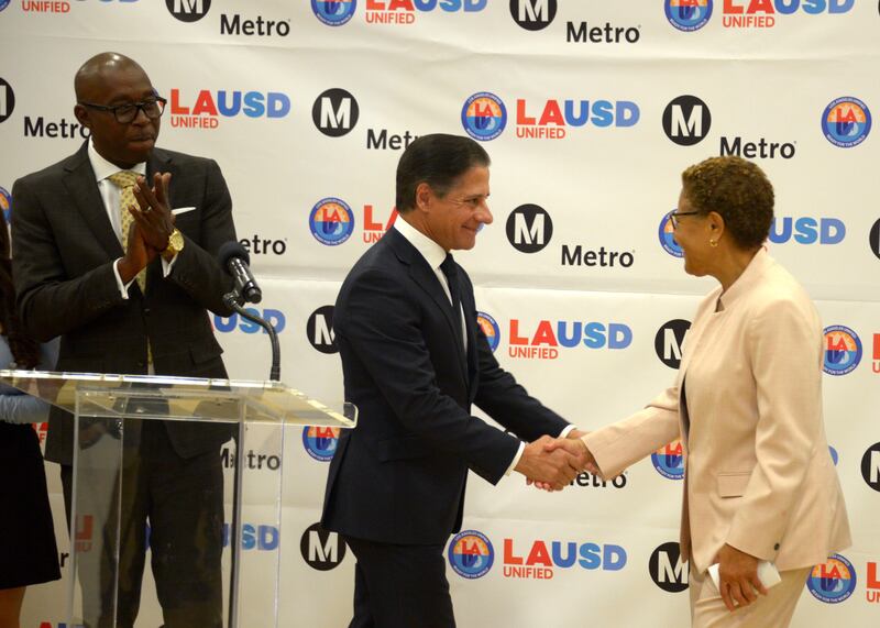 L.A. Mayor Karen Bass (right) and LAUSD Superintendent Alberto Carvalho (center) shake hands at a press conference in front of a LAUSD and LA Metro backdrop.