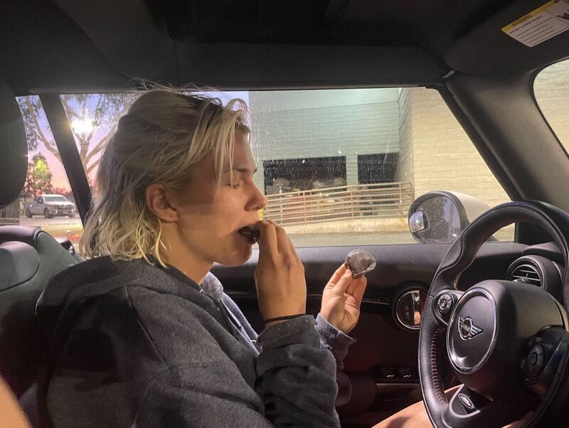 Light smiles as she bites into a Reese's Peanut Butter Cup. She is sitting in a black mini cooper.
