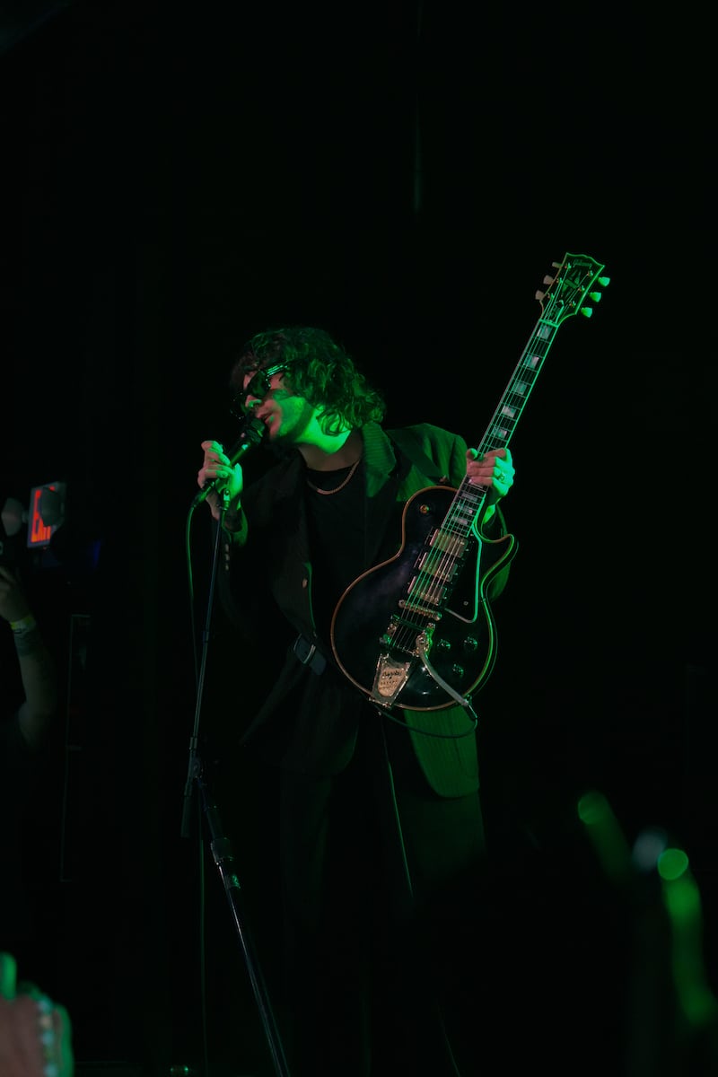 Holiday is covered by green light and holds his guitar.