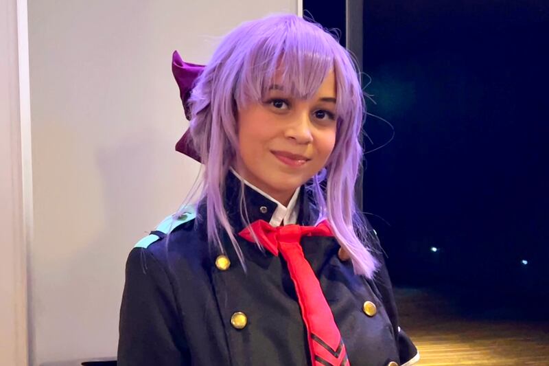 Claire Sullivan poses in front of the concert hall entrance, wearing a purple wig and a uniform resembling the character's.