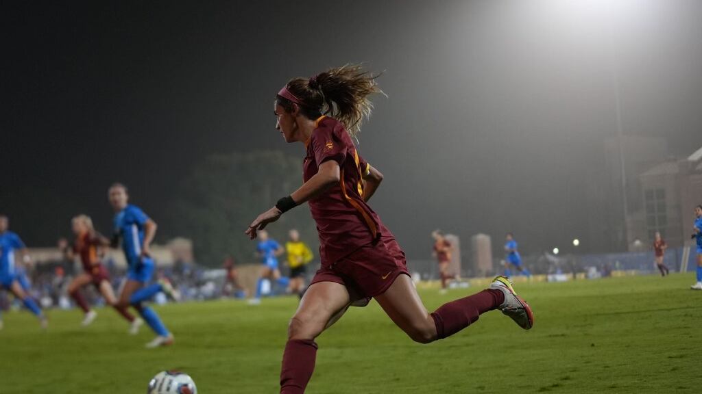 Savannah DeMelo in a red jersey plays the ball forward in a game against UCLA.