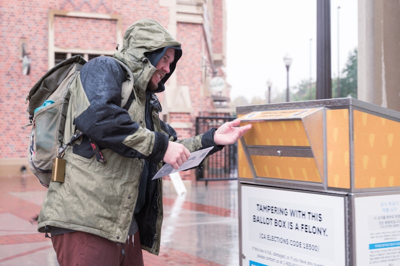 A student drops his vote into the ballot box at the USC Village while weathering the rain on Election Day before the polls close. (Photo by Michael Chow)