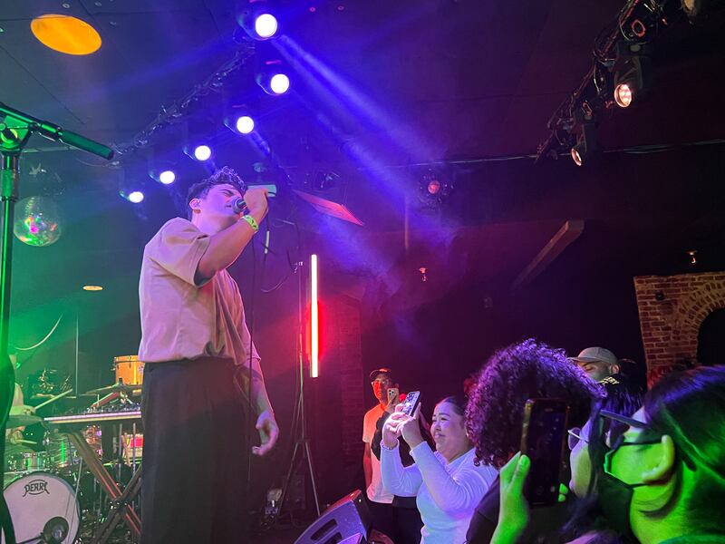 Photo of a man singing on stage as a fan takes a photo