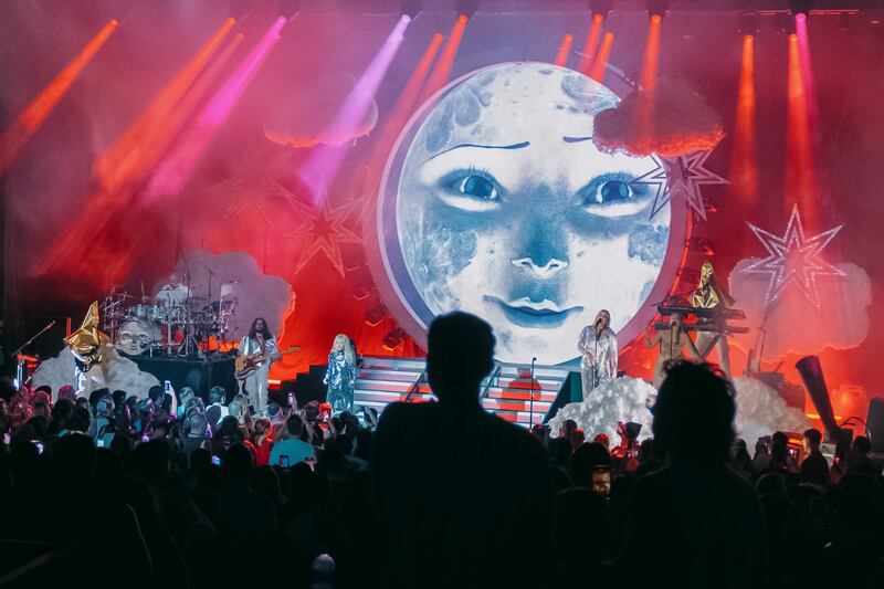 A photo of Jepsen and her band members on stage with a giant animated moon with a face on the stage's backdrop.
