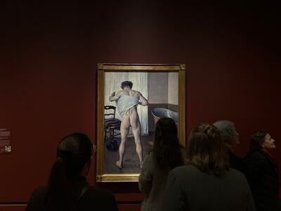 People stand and look at the painting. It is against a red wall and in a gold frame.