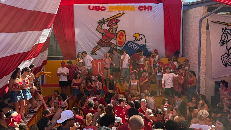 Tailgaters gather under a large banner depicting Tommy Trojan slaying GSU's Eagle and that reads "USC SIGMA CHI"