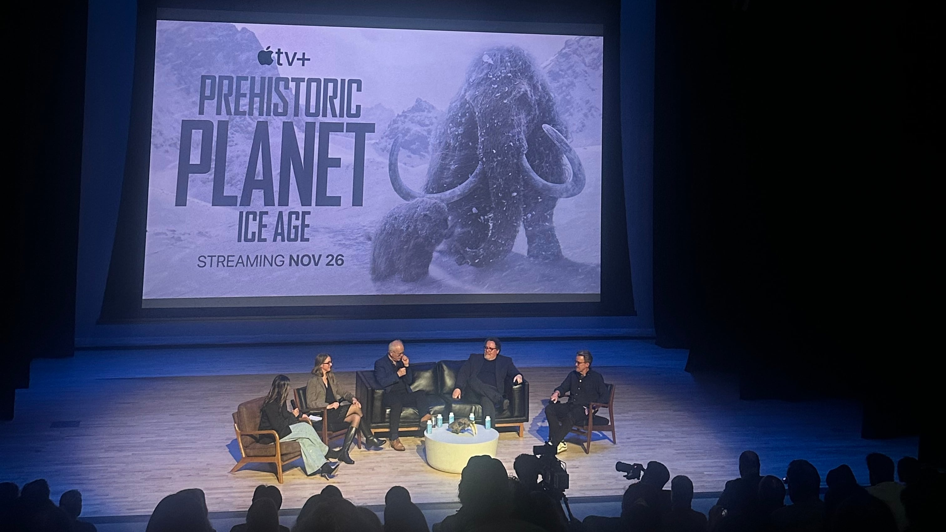 Five panelists sit onstage at a theater within the Natural History Museum, with the large screen behind them displaying the words "Prehistoric Planet: Ice Age" and a photo of a giant mammoth.