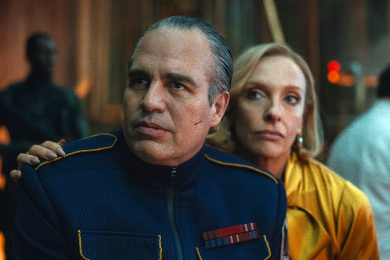 Film still of a man with gray hair in a blue uniform next to a woman in yellow