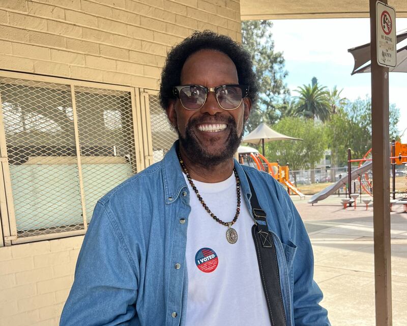 A man with sunglasses and a beaded necklace smiling at the camera.