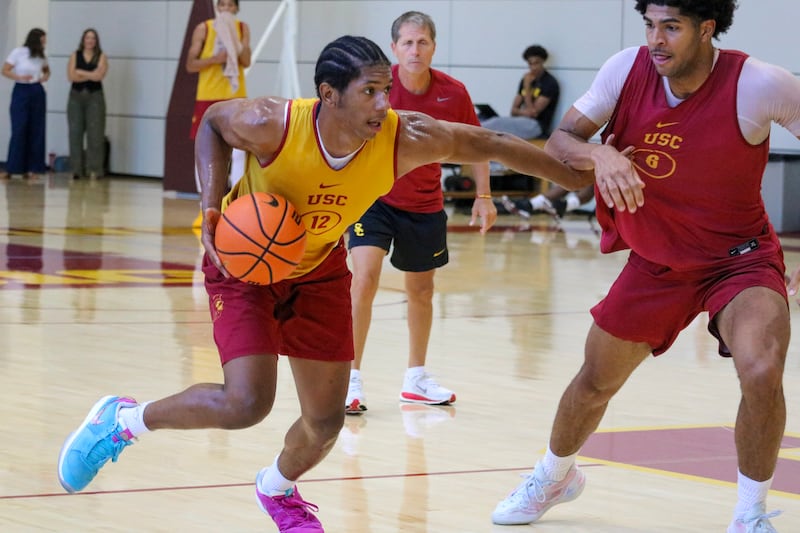 Jerry Easter II (8) drives with basketball in hand while defended by Jacob Cofie (6). Easter II wears a gold basketball practice jersey with cardinal accents, while Cofie wears a cardinal jersey with gold accents. Head coach Eric Musselman watches intently from the background.