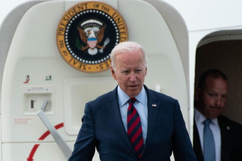 White haired man in suit walking off plane.