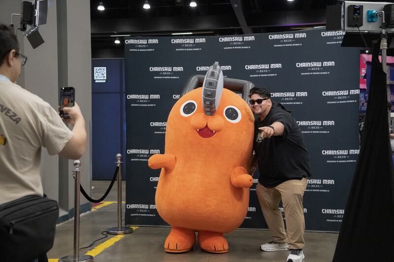 Photo of an attendee in sunglasses poses for a photo with a cosplayer in an orange Pochita costume.