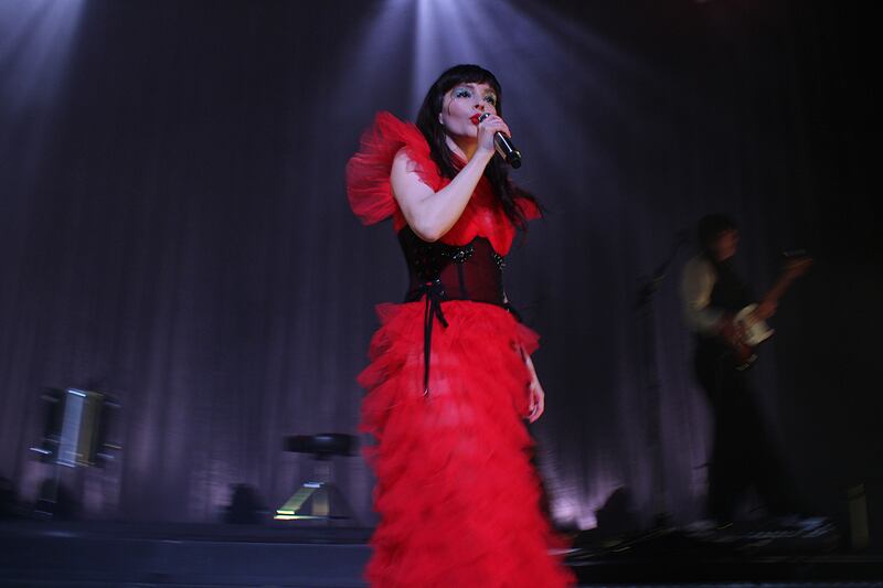 Photo of a woman wearing a red dress holding a microphone in front of a black background