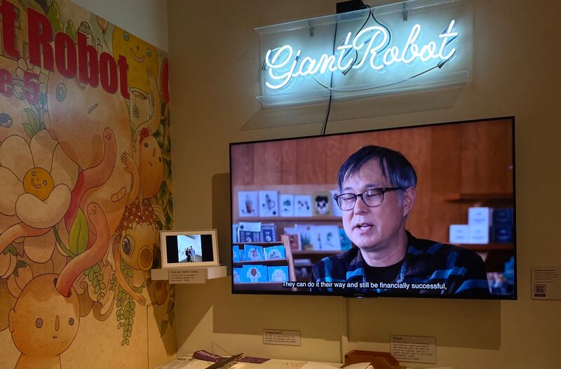 Photo of a TV screen with a man and a neon sign saying "Giant Robot"