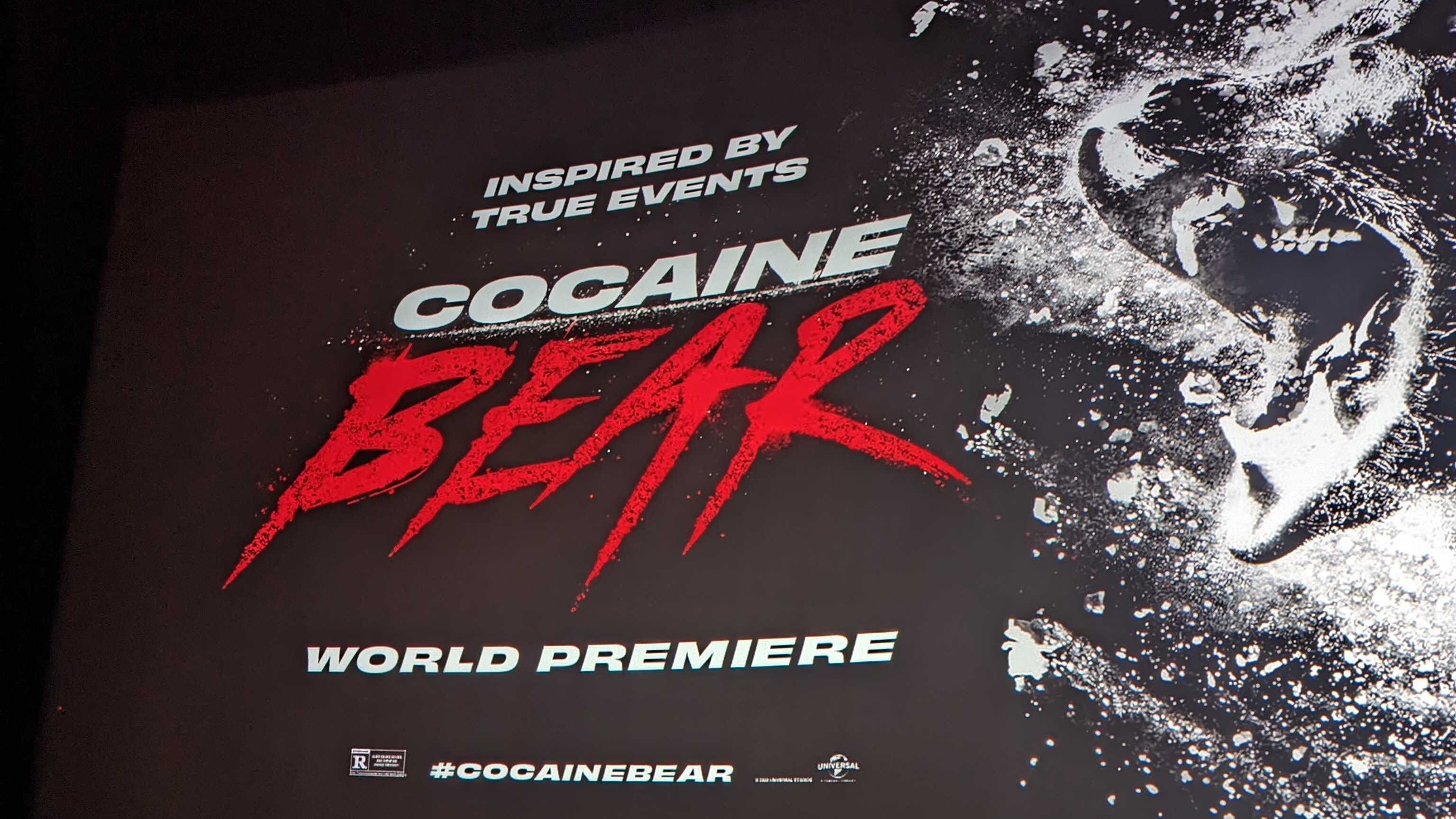 A photo of the screen in a movie theater with the "Cocaine Bear" title screen and the promotional image of the bear.