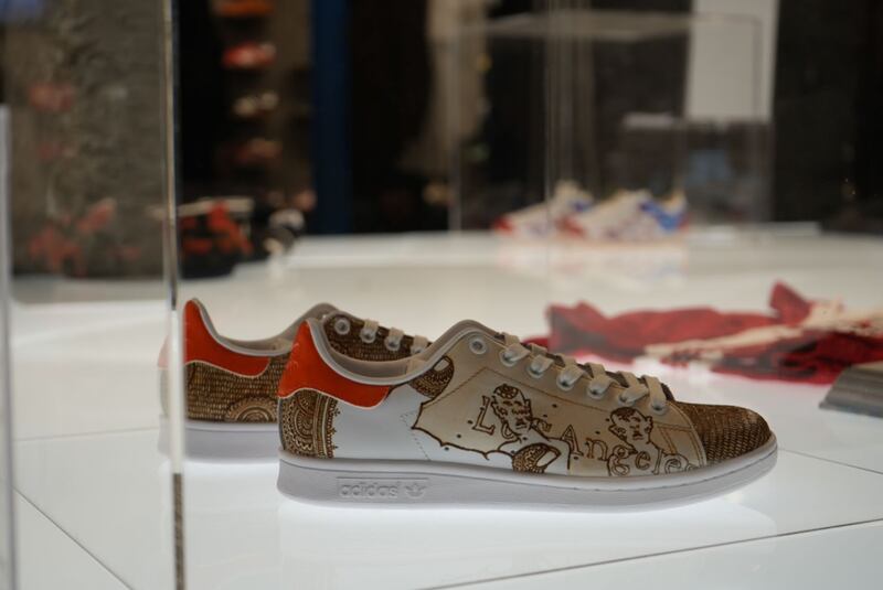 The sneakers are in a glass case. They are Adidas shoes with brown henna designed and read Los Angeles across. The back of the shoes are orange