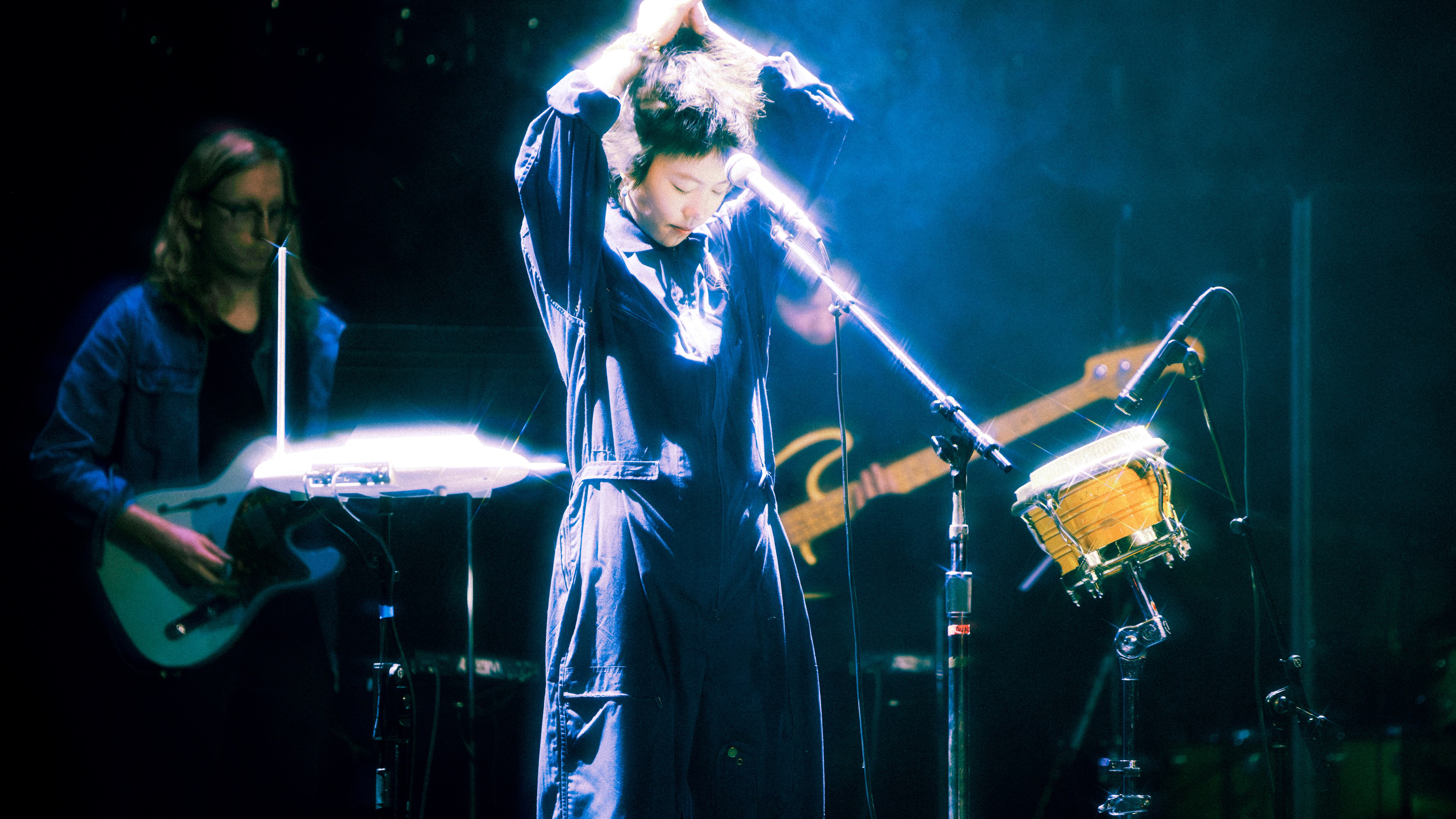 Photo of a woman in front of a microphone with her hands clasped together in the air