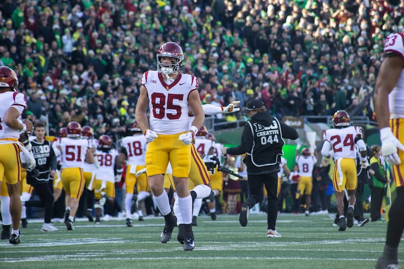 USC's Walker Lyons (85) jumps in the air to get teammates pumped pregame. He wears a white football jersey and cardinal helmet with gold pants.