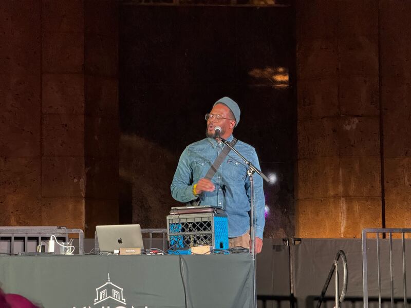 A rapper in all denim plays a set on stage in front of a microphone.