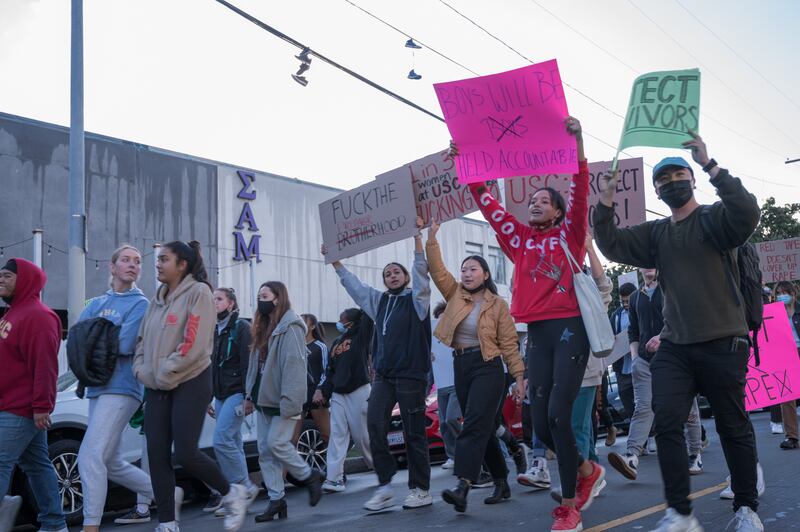 Students march in protest with a sign reading “Abusers will be held accountable."