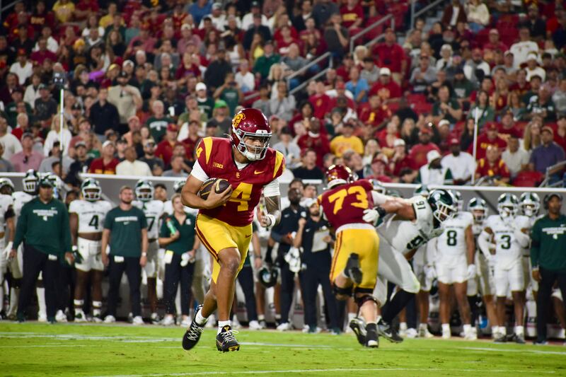 Jayden Maiava (14) sneaks the ball up the football field. He wears a cardinal and gold USC football uniform.