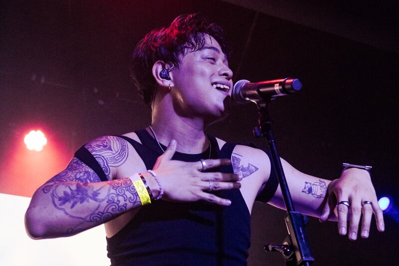 Photo of a man with tattoos singing into a microphone with one hand on his chest