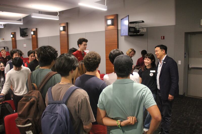 Photo of a group of students crowding around a man with a suit