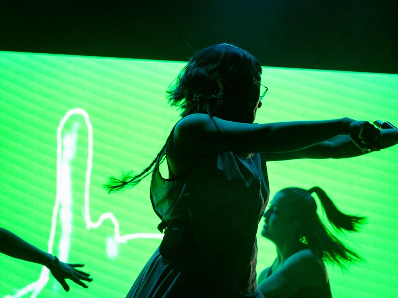 Photo of a woman dancing in front of a bright green LED screen