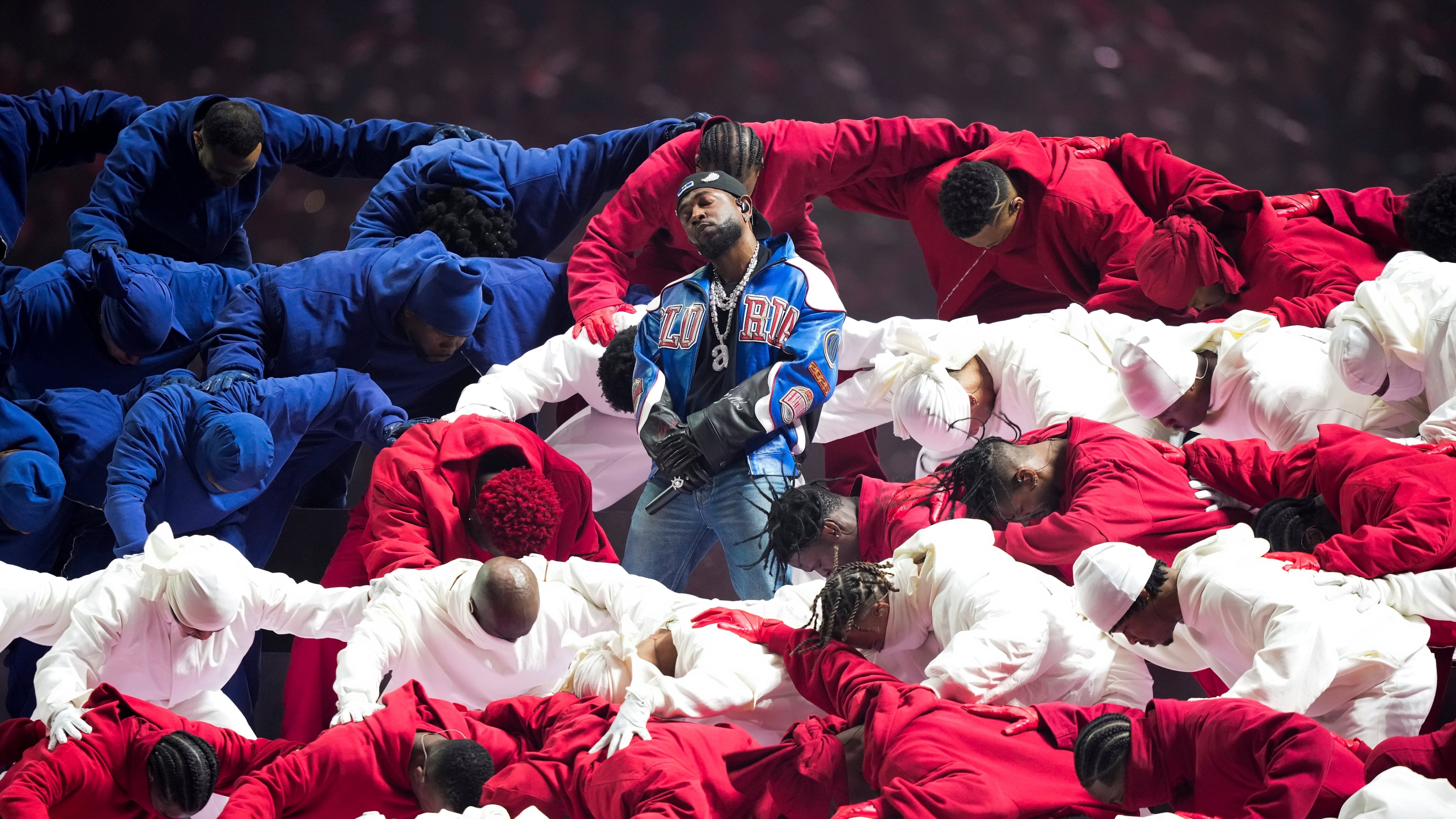 Kendrick Lamar stands amongst dancers in red, white and blue costumes emulating the American flag.