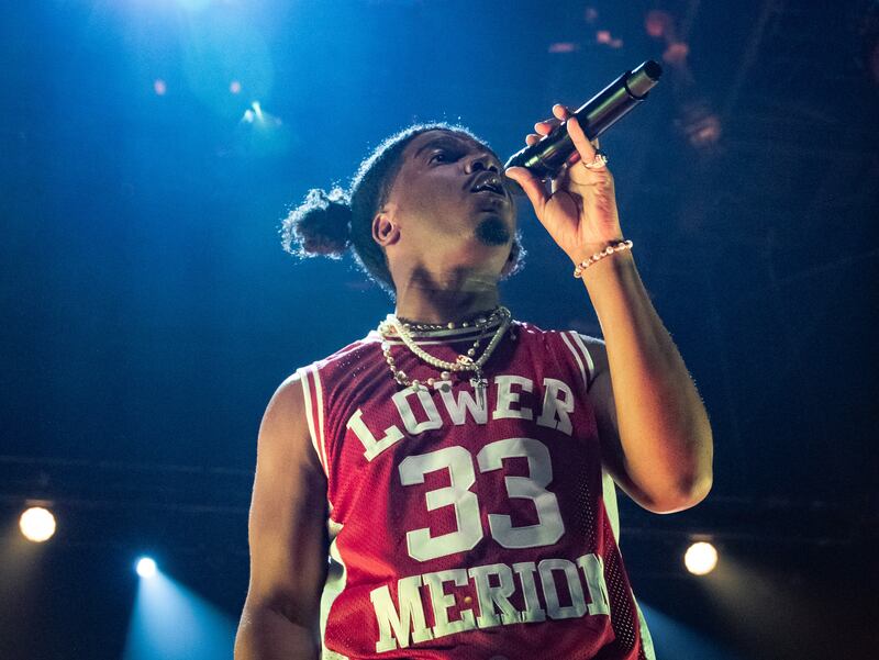 A photo of Smino singing into the microphone. His shirt says “Lower Merion” and has the number 33 on it.