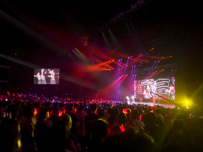 Photo of a crowd of people with red light sticks in front of a stage