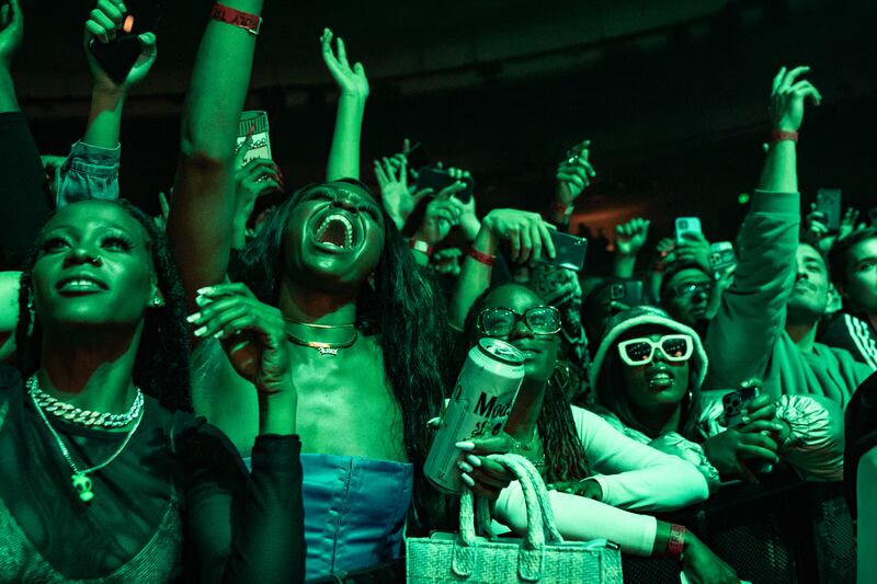 A photo of members of the crowd jumping, singing and dancing along to the music. There is a green light washing over them.