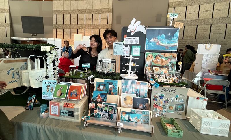 Photo of two people standing behind a booth with artwork on display