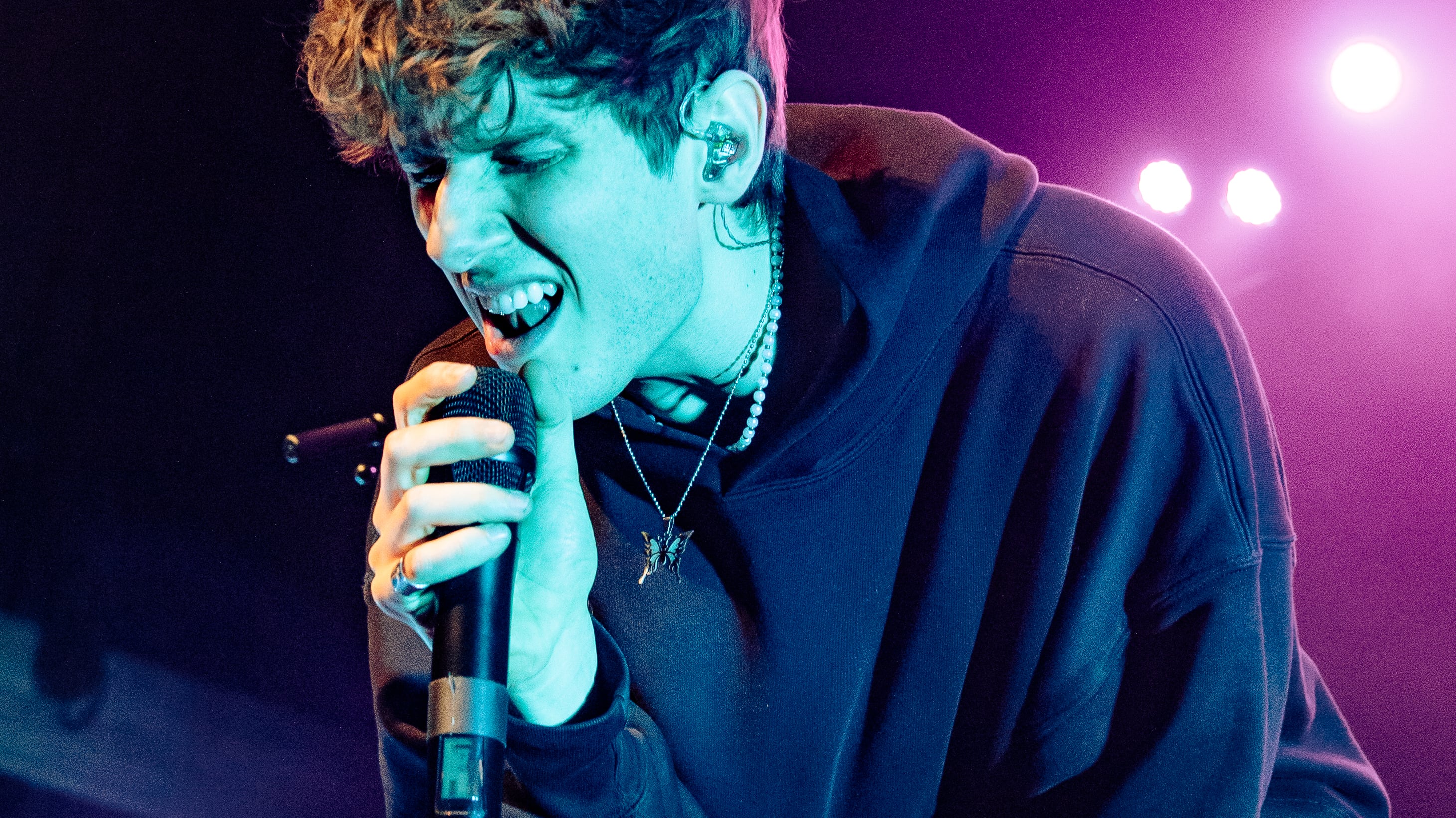 A photo of JVKE singing into the microphone while hunched over on stage.