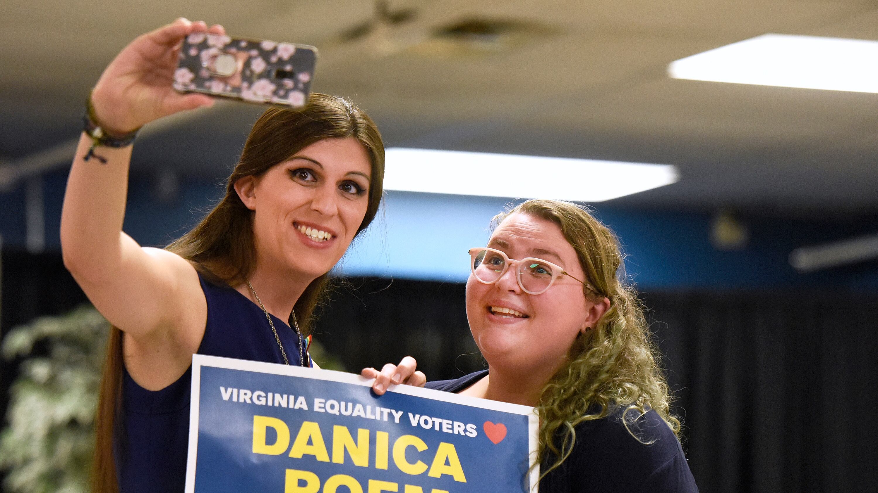 Photo of two femmes taking selfie with campaign poster.