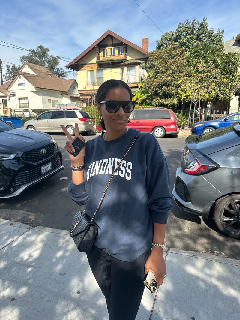 A woman in sunglasses and a sweatshirt holding up a peace sign.