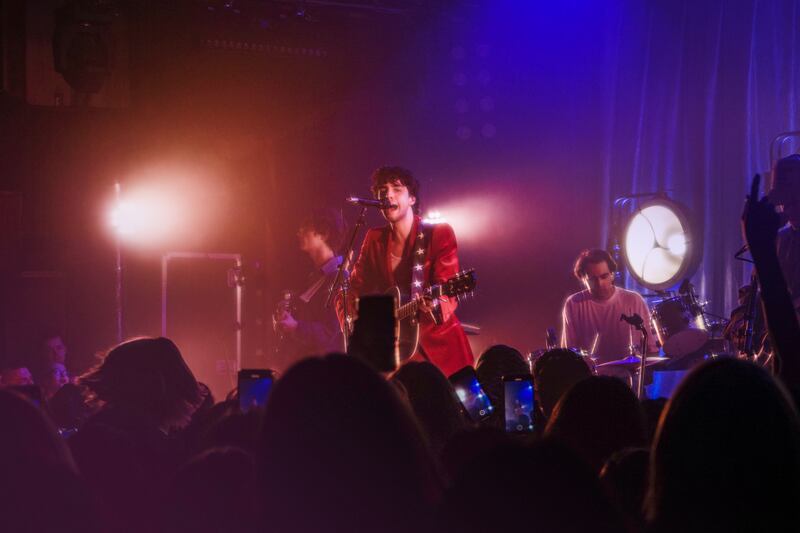 A photo of Sanchez playing guitar and singing into a microphone onstage.