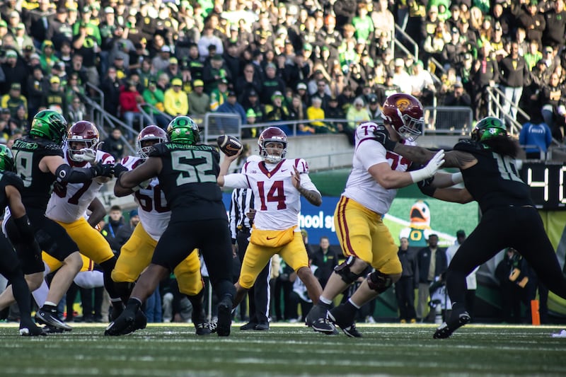 Centers on Jayden Maiava with football in hand in a throwing motion. USC and Oregon players can be seen surrounding him.