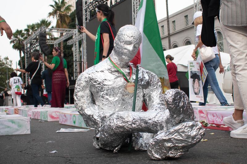The sculpture of a person with their arms and legs wrapped around the Red Lion and Sun flag.