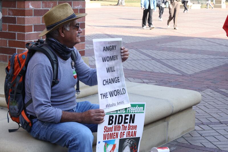 Man sitting and holding a sign saying "Angry Women Will Change The World"