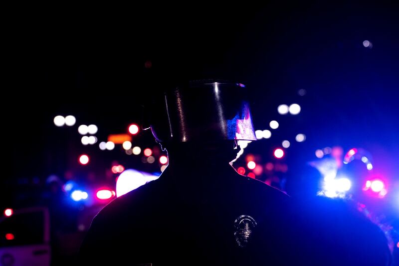 [A photo of a police officer backlit by police lights.]