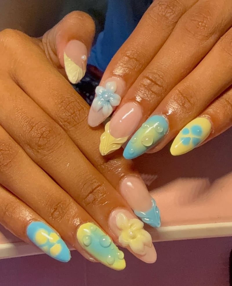 Hands with yellow and blue press on nails. The nails have 3D elements like flowers and fake water droplets.