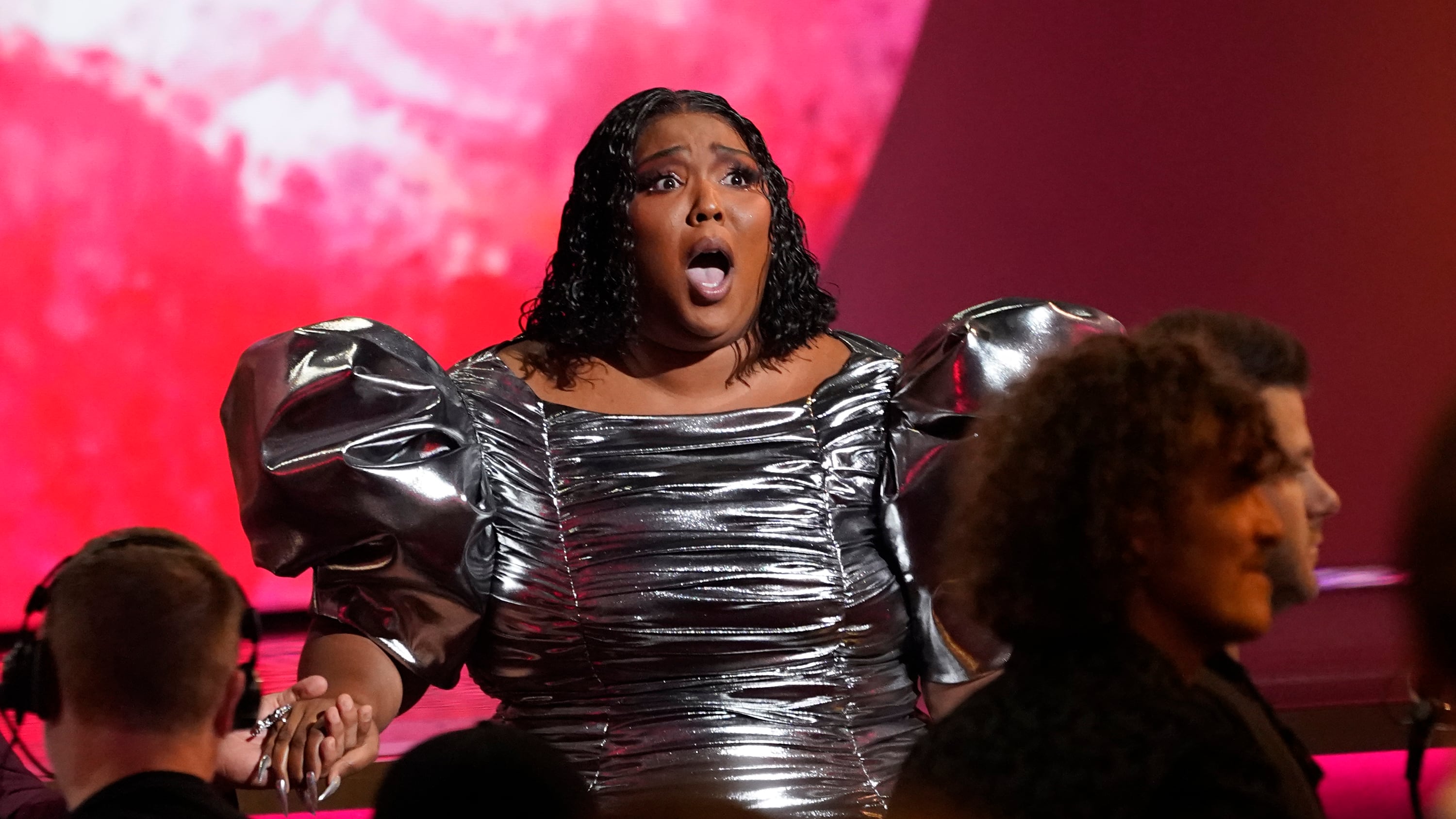 A photo of Lizzo in a silver dress with a shocked look on her face