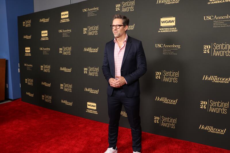 Todd is wearing glasses, a navy blue suit and a pink undershirt.