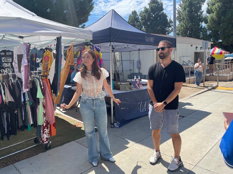 Photo of a woman next to a man in front of a booth with clothes