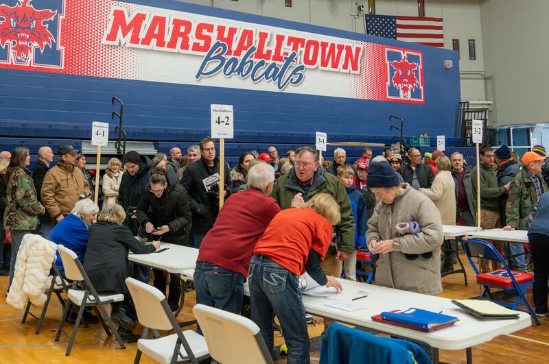 A group at the Iowa Caucus gathered around white foldable tables.