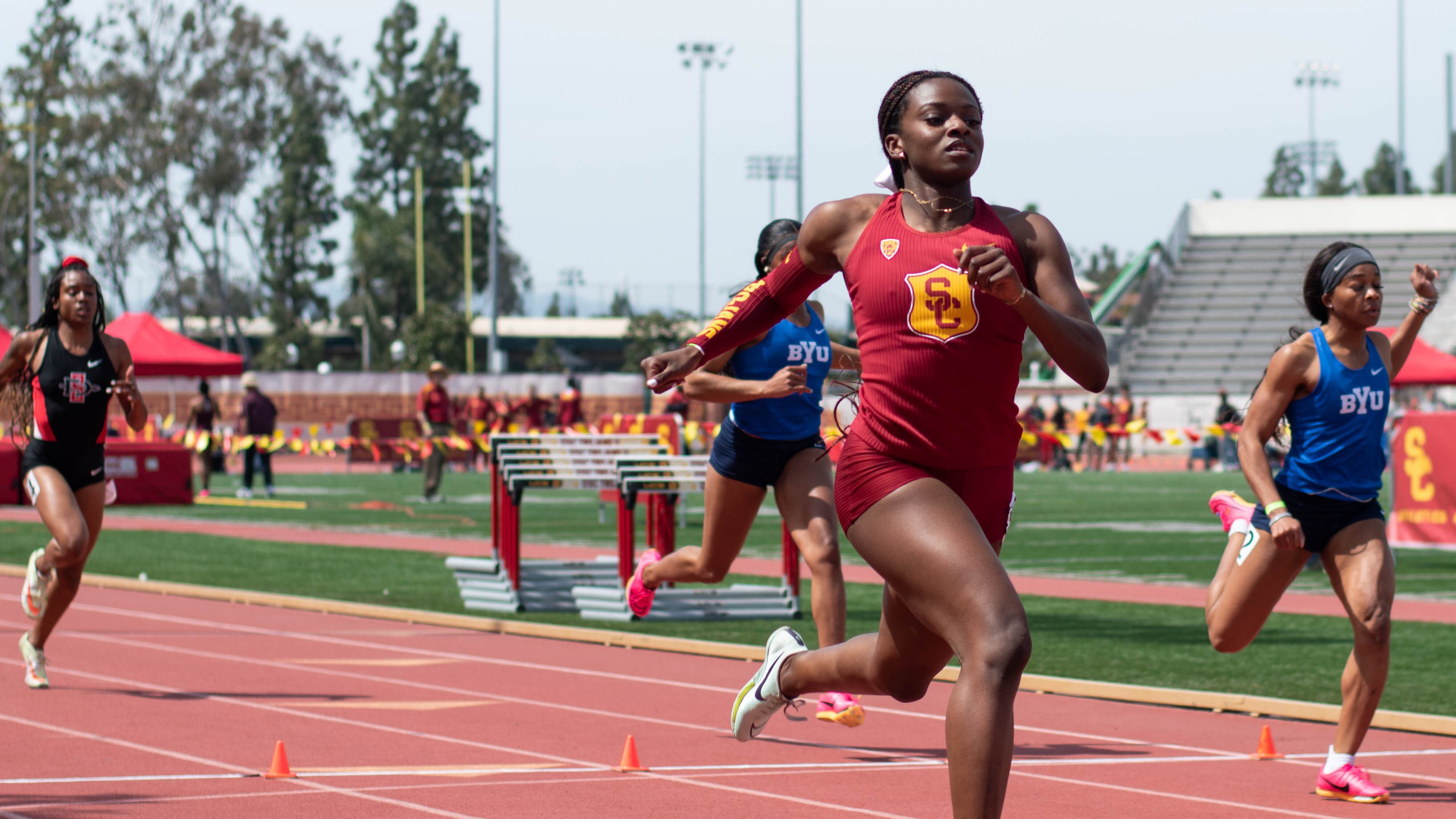 A sprinter is finishing the race. She is wearing a cardinal uniform.