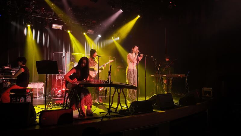 Photo of a woman on stage with an instrument in front of a band under yellow lights
