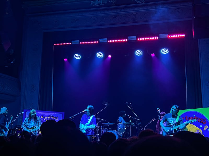 Photo of three people with guitars on a starge under dark blue lights
