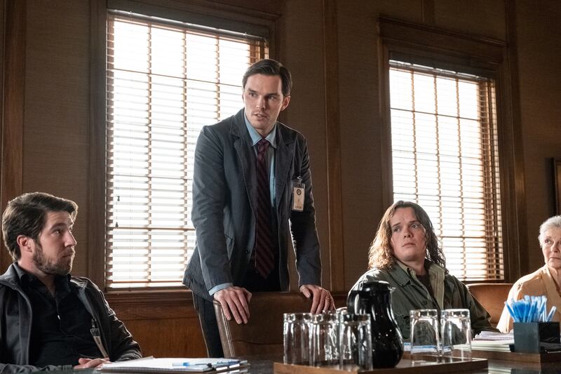 Film still of a man with a suit and tie standing by a table talking to a group of people